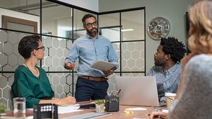 Mitarbeiter präsentiert einer Arbeitsgruppe im Besprechungsraum ein Dokument.