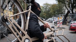 Vermummte Person trägt ein Fahrrad auf einer Straße davon.
