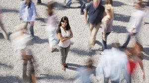 Frau steht still in einer belebten Fußgängerzone, während Menschen an ihr vorbeigehen.