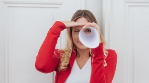 Frau blickt durch ein zusammengerolltes Blatt Papier wie durch ein Fernrohr.