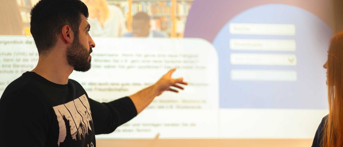Student hält vor einer projizierten Präsentation einen Vortrag.