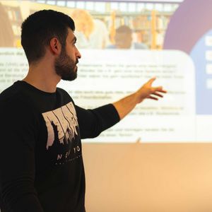 Student hält vor einer projizierten Präsentation einen Vortrag.
