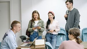 Studierende stehen und sitzen in einem Seminarraum und diskutieren miteinander.