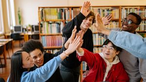 Gruppe von Lernenden gibt sich in einer Bibliothek gegenseitig ein High Five.
