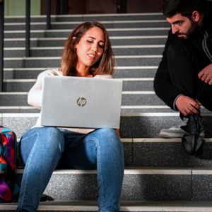 Zwei Studierende sitzen auf einer Treppe und arbeiten gemeinsam an einem Laptop.
