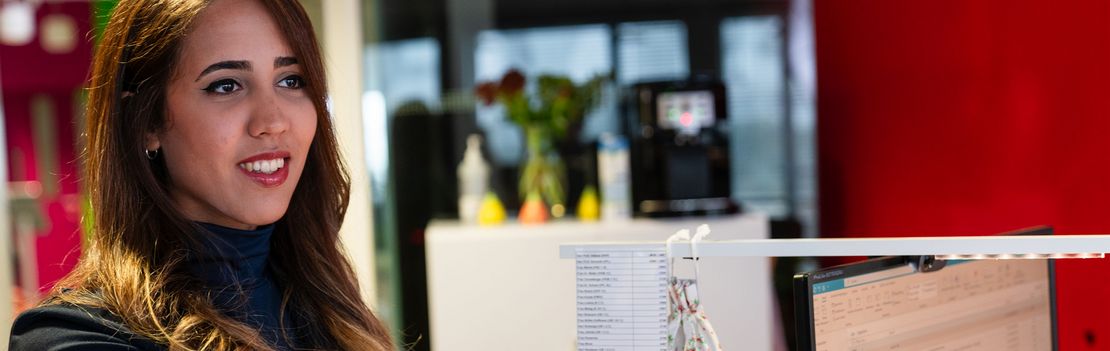 Eine junge Frau wird per Handschlag im Empfangsbereich eines Unternehmens begrüßt.