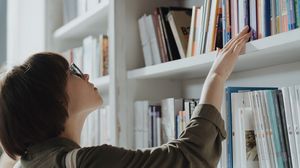 Studentin greift in einer Bibliothek nach einem Buch im Regal.