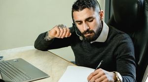 Mann telefoniert am Schreibtisch und macht sich dabei Notizen.