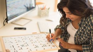 Frau trägt Termine in einen großen Kalender auf ihrem Schreibtisch ein.