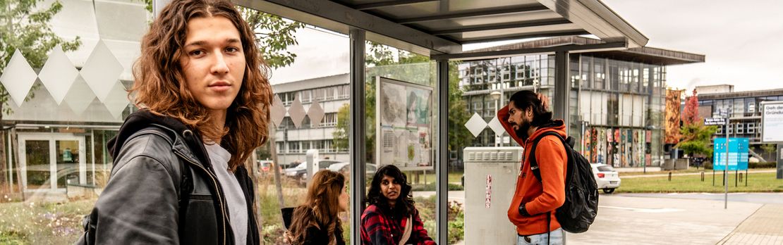 Vier Studierende warten auf dem Campus der BTU an einer Bushaltestelle auf ihre Verbindung.