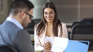 Bewerberin sitzt lächelnd einem Gesprächspartner bei einem Vorstellungsgespräch gegenüber.