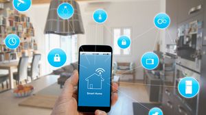Hand hält ein Smartphone mit einer Smart-Home-Anwendung; darüber sind Symbole vernetzter Geräte eingeblendet.
