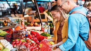 Junges Paar sucht gemeinsam frisches Gemüse an einem Marktstand aus.