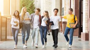 Gruppe junger Erwachsener geht lachend und miteinander sprechend über einen Campus.