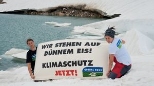 Zwei Klimaaktivisten knien auf einer Eisfläche und halten ein Plakat mit der Aufschrift „Wir stehen auf dünnem Eis! Klimaschutz jetzt!“.