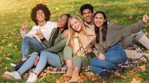 Vier junge Erwachsene sitzen gut gelaunt auf einer Decke in einem herbstlichen Park.