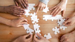 Mehrere Personen legen gemeinsam weiße Puzzleteile auf einem Holztisch zusammen.