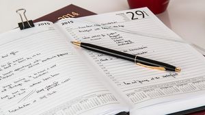 Aufgeschlagener Terminkalender mit handschriftlichen Einträgen und einem Stift.