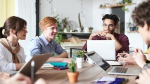 Fünf Studierende arbeiten mit Laptops und Unterlagen gemeinsam an einem Tisch.