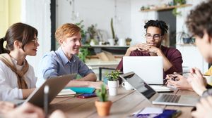 Fünf Studierende arbeiten mit Laptops und Unterlagen gemeinsam an einem Tisch.
