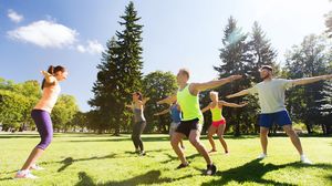 Gruppe macht gemeinsam Gymnastikübungen auf einer Wiese im Park.