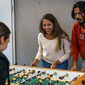 Drei junge Erwachsene spielen gemeinsam an einem Tischkicker.