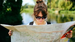 Junge Frau mit Sonnenbrille liest im Freien in einer großen Landkarte.
