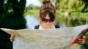 Junge Frau mit Sonnenbrille liest im Freien in einer großen Landkarte.
