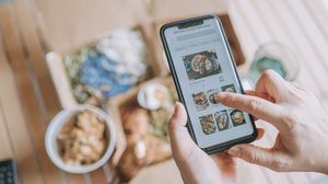 Person wählt auf einem Smartphone Gerichte bei einem Online-Lieferdienst aus.